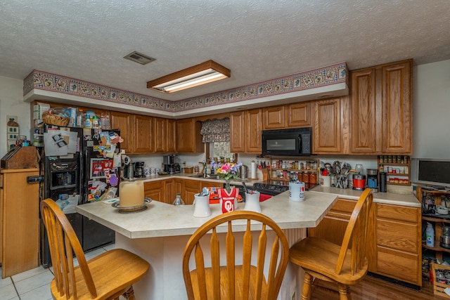 kitchen with a breakfast bar area, kitchen peninsula, a textured ceiling, and black appliances