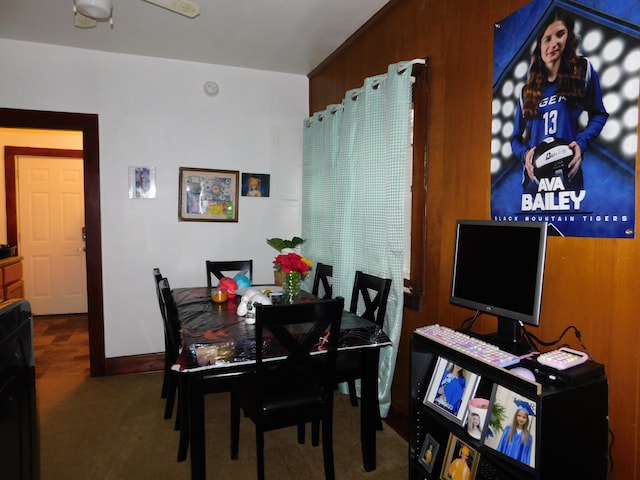 dining area featuring carpet flooring, wood walls, and ceiling fan