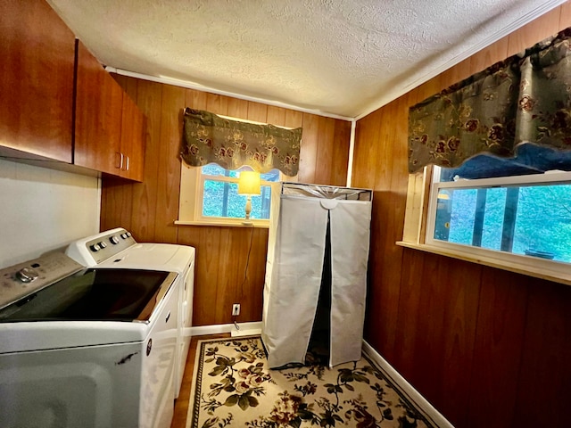 clothes washing area featuring washer and clothes dryer, cabinets, a textured ceiling, and wood walls