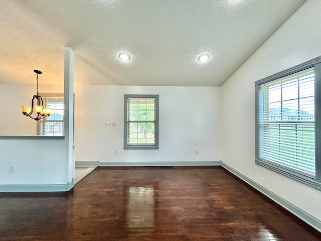 empty room with a textured ceiling, vaulted ceiling, dark hardwood / wood-style floors, and plenty of natural light