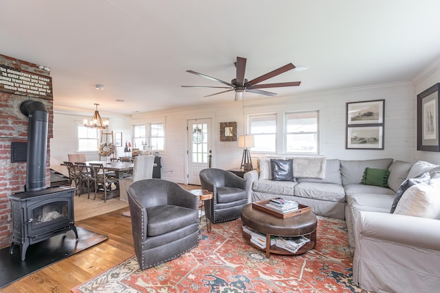 living room featuring ceiling fan with notable chandelier, a wood stove, ornamental molding, and hardwood / wood-style floors