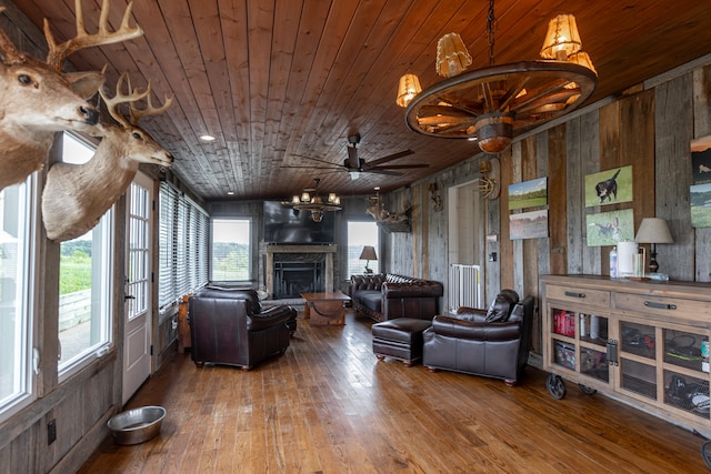 living room with ceiling fan with notable chandelier, wood ceiling, wooden walls, and hardwood / wood-style flooring