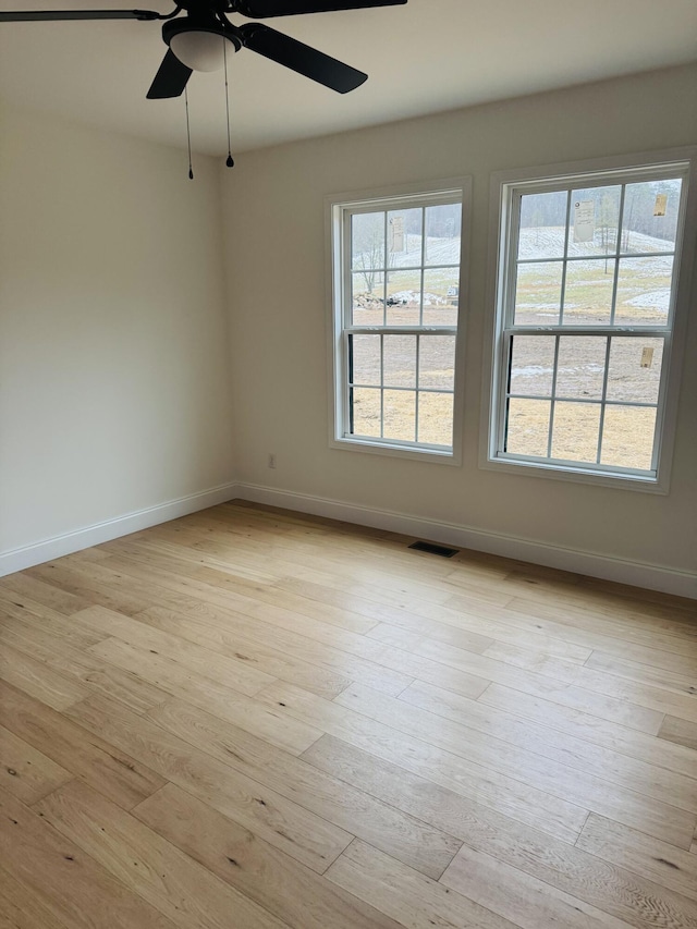 empty room with ceiling fan, a wealth of natural light, and light hardwood / wood-style flooring