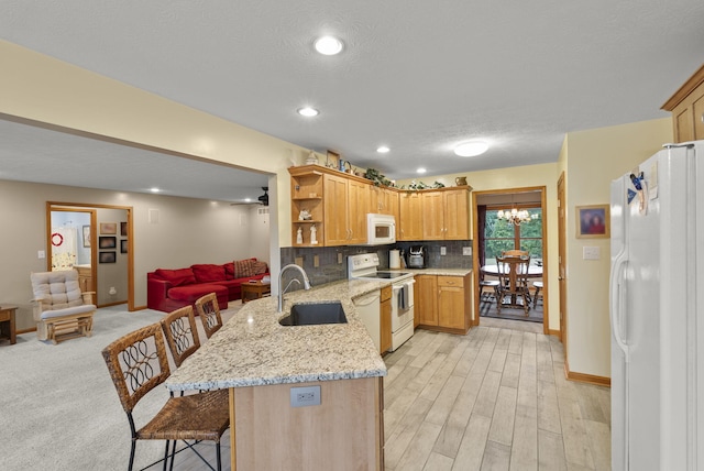 kitchen with kitchen peninsula, sink, white appliances, a breakfast bar, and light hardwood / wood-style floors