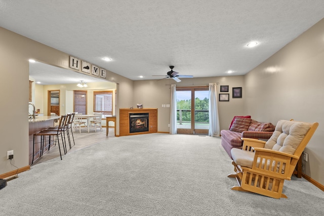 living room featuring a textured ceiling, ceiling fan, light colored carpet, and a brick fireplace