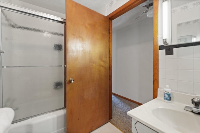 bathroom featuring vanity, combined bath / shower with glass door, and a textured ceiling