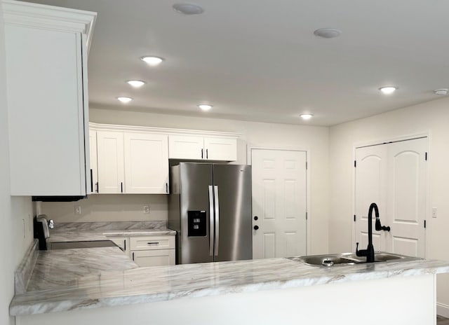 kitchen featuring white cabinetry, sink, kitchen peninsula, stainless steel fridge, and range