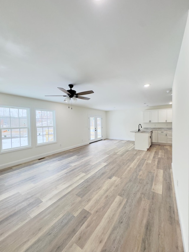 unfurnished living room featuring ceiling fan, sink, french doors, and light wood-type flooring