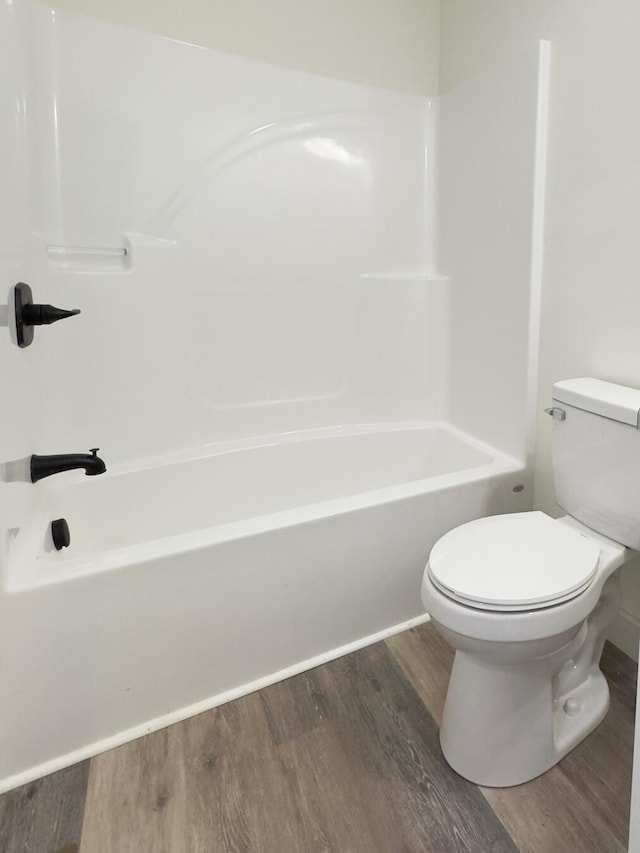 bathroom featuring hardwood / wood-style floors, washtub / shower combination, and toilet