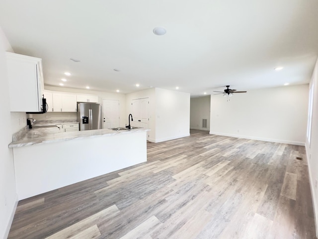 kitchen with kitchen peninsula, stainless steel refrigerator with ice dispenser, light hardwood / wood-style flooring, and white cabinetry