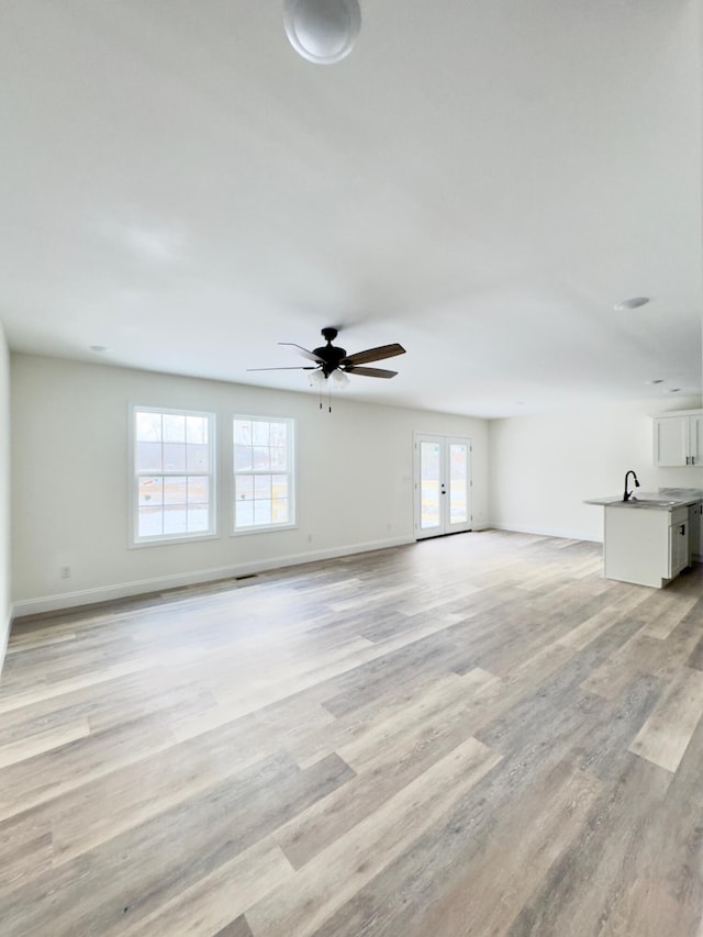 unfurnished living room with french doors, light hardwood / wood-style floors, ceiling fan, and sink