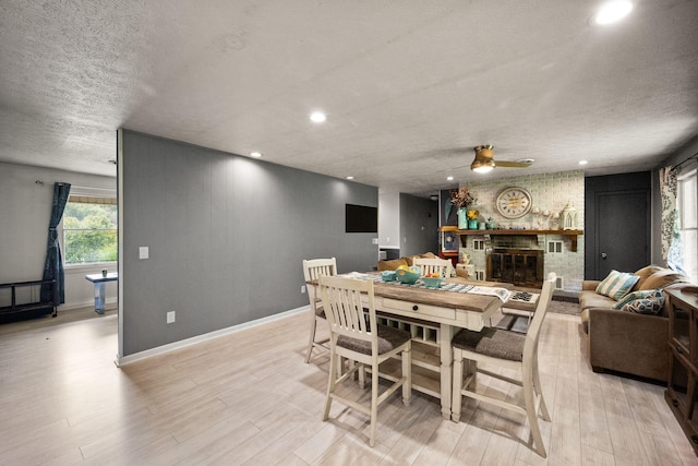 dining room featuring light wood-type flooring, a textured ceiling, ceiling fan, and a brick fireplace