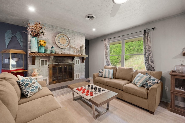 living room with a textured ceiling, light hardwood / wood-style floors, a fireplace, and ceiling fan