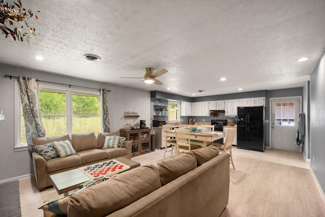 living room with light hardwood / wood-style flooring, a textured ceiling, and ceiling fan