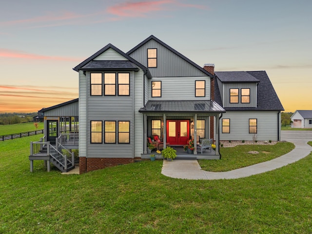 back house at dusk with covered porch, a yard, and french doors