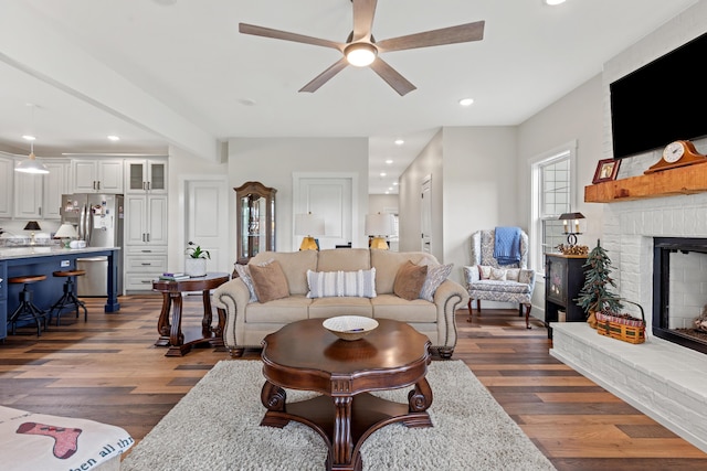 living room featuring beamed ceiling, dark hardwood / wood-style flooring, a brick fireplace, and ceiling fan