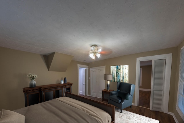 bedroom featuring a textured ceiling, ceiling fan, dark wood-type flooring, and multiple closets