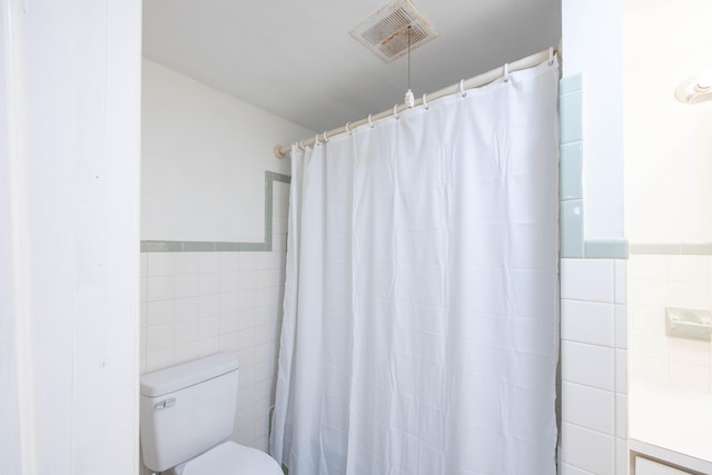 bathroom with curtained shower, toilet, and tile walls