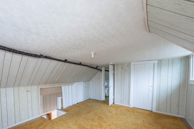 bonus room with carpet, a textured ceiling, wooden walls, and vaulted ceiling