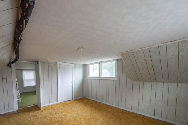 bonus room with light colored carpet, lofted ceiling, a textured ceiling, and wooden walls