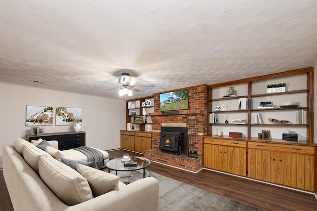 living room featuring hardwood / wood-style floors, ceiling fan, a wood stove, and a textured ceiling