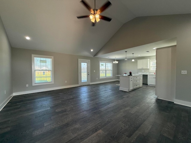 unfurnished living room with a wealth of natural light, dark hardwood / wood-style flooring, high vaulted ceiling, and ceiling fan with notable chandelier