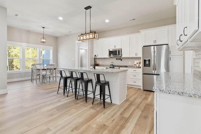 kitchen featuring tasteful backsplash, a center island with sink, light wood-style flooring, a kitchen breakfast bar, and stainless steel appliances