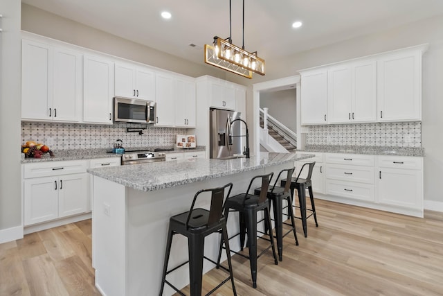 kitchen featuring a breakfast bar, light wood finished floors, stainless steel appliances, tasteful backsplash, and white cabinets