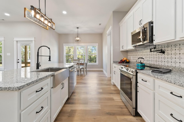 kitchen with stainless steel appliances, tasteful backsplash, white cabinetry, a sink, and light wood-type flooring