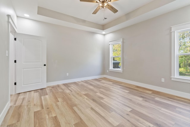 empty room with ceiling fan, a raised ceiling, light wood-style flooring, and baseboards