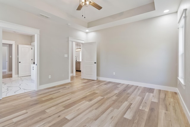 unfurnished bedroom featuring a raised ceiling, light wood finished floors, and baseboards