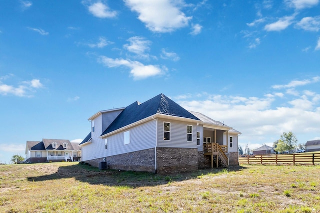 view of side of home featuring brick siding, a lawn, central AC unit, and fence