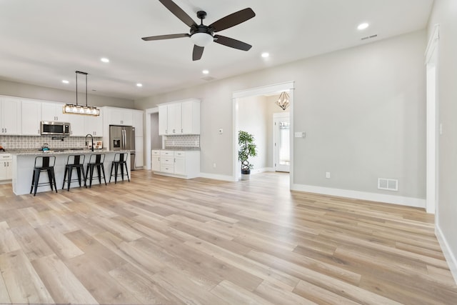 unfurnished living room featuring light wood-type flooring, baseboards, visible vents, and a sink