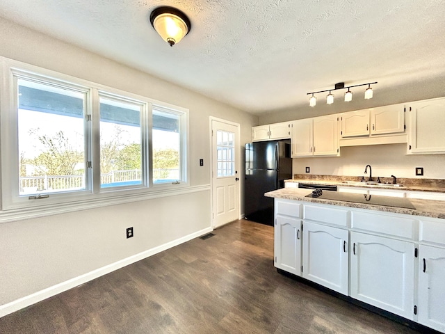 kitchen featuring black refrigerator, dark wood-type flooring, light stone counters, sink, and white cabinetry