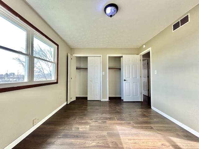 unfurnished bedroom featuring multiple closets and dark wood-type flooring