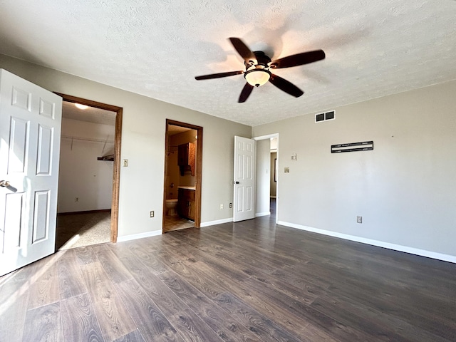 unfurnished bedroom featuring ensuite bathroom, a closet, dark hardwood / wood-style flooring, a walk in closet, and ceiling fan