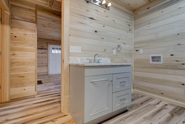 laundry room with hookup for a washing machine, light hardwood / wood-style flooring, and wooden walls