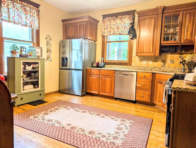 kitchen featuring tasteful backsplash, light stone countertops, stainless steel appliances, and light hardwood / wood-style flooring