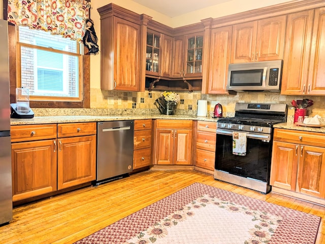 kitchen with appliances with stainless steel finishes, light hardwood / wood-style flooring, tasteful backsplash, and light stone countertops