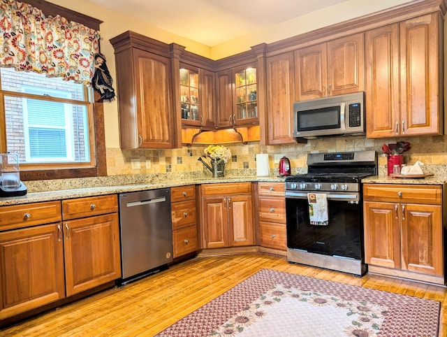 kitchen featuring decorative backsplash, light stone countertops, appliances with stainless steel finishes, and light hardwood / wood-style flooring