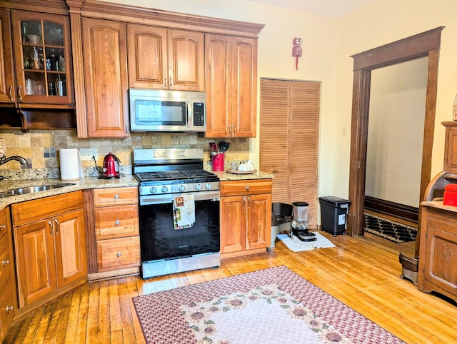 kitchen featuring stainless steel appliances, tasteful backsplash, sink, light wood-type flooring, and light stone counters