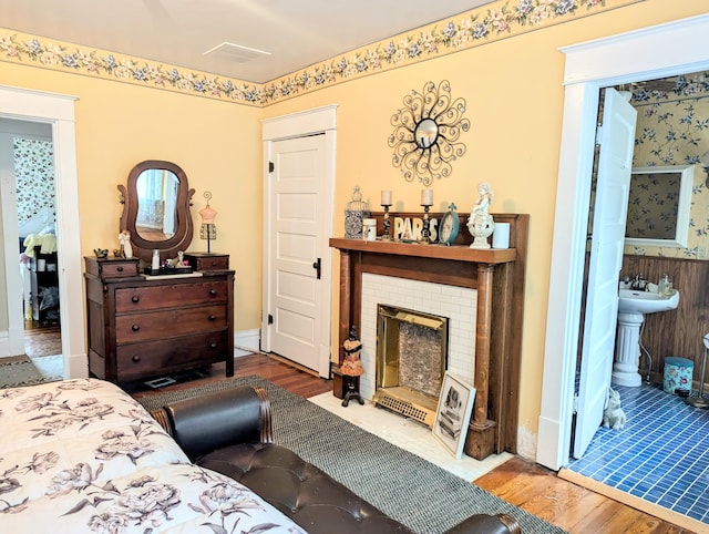 bedroom with ensuite bath, a brick fireplace, sink, and hardwood / wood-style flooring