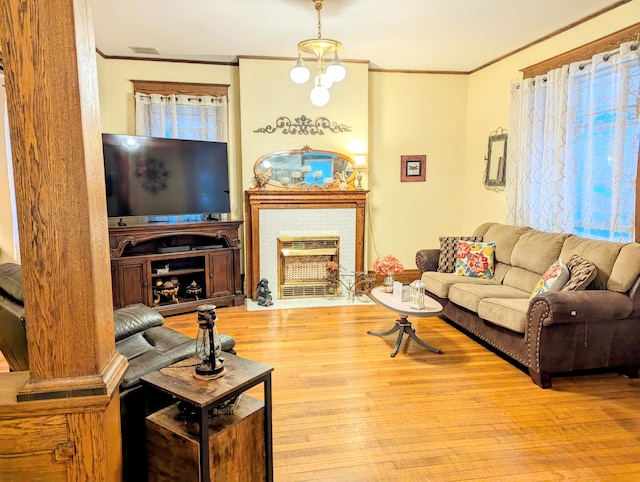 living room featuring a brick fireplace, crown molding, light hardwood / wood-style floors, and an inviting chandelier