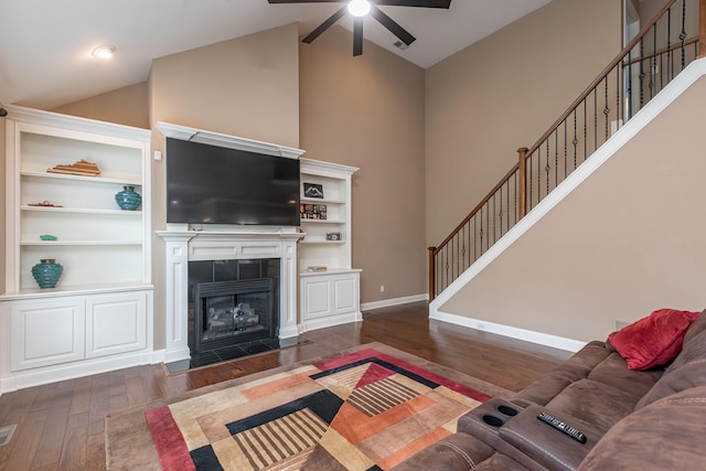 living room featuring dark wood-type flooring, high vaulted ceiling, a fireplace, ceiling fan, and built in shelves