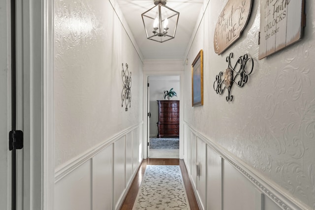 hall with wood-type flooring, ornamental molding, and a notable chandelier