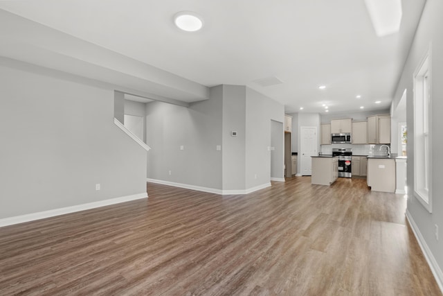 unfurnished living room featuring baseboards, recessed lighting, a sink, and light wood-style floors