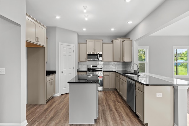 kitchen with dark countertops, a kitchen island, appliances with stainless steel finishes, a peninsula, and a sink