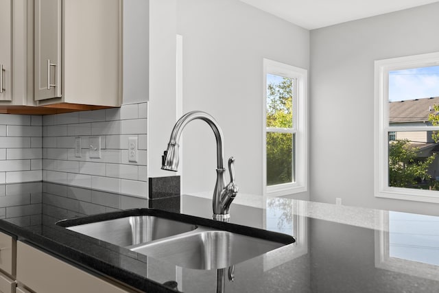 kitchen with dark stone countertops, decorative backsplash, and a sink