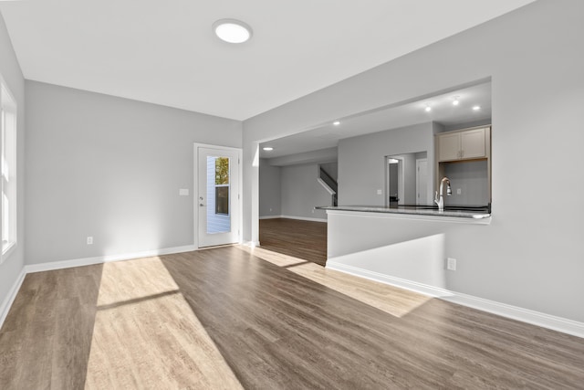 unfurnished living room with a sink, stairway, wood finished floors, and baseboards