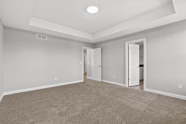 unfurnished bedroom with visible vents, a tray ceiling, and carpet flooring